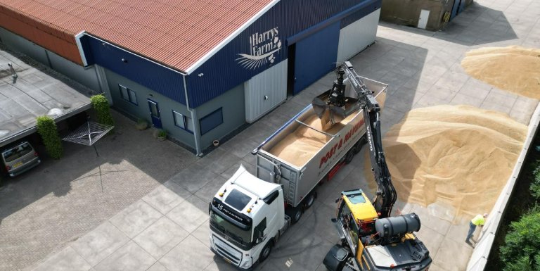 Een witte vrachtwagen van Post & Haveman wordt bij een boerderij geladen