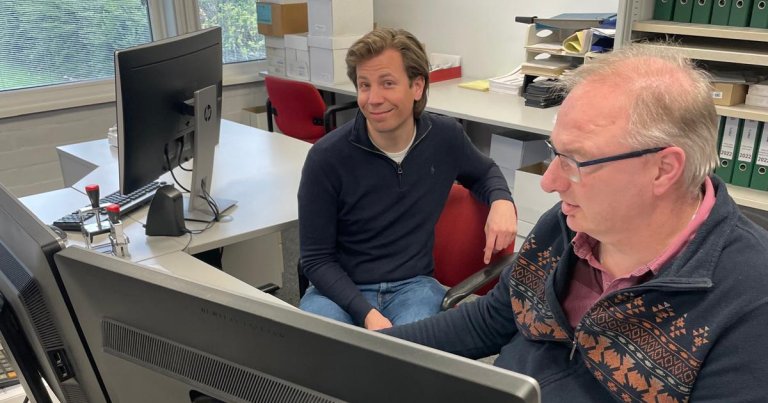 Twee personen van P&H achter een bureau / monitor.